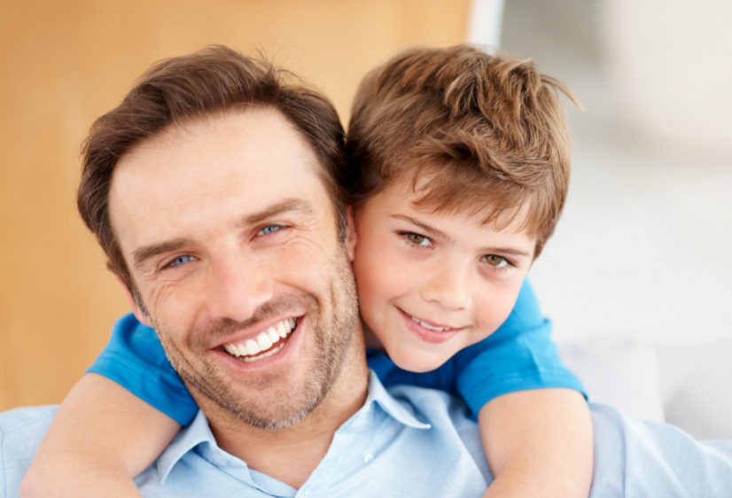 Picture of father smiling, with young son hugging him around the neck