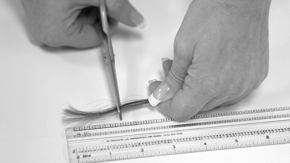 Black and white image of woman cutting hair by a ruler